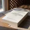 El Recuerdo de los Estados de los Muertos y los Asuntos de la Otra Vida (Tomo 2 - Edición bilingüe) de Imam al Qurtubi, sobre una mesa de madera con la sombra de una celosía